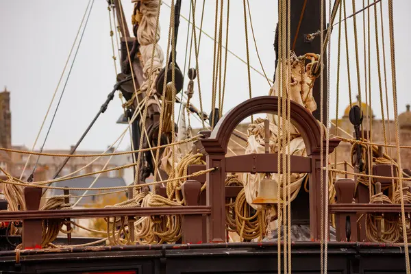 Yakın plan bir gemi donanımı, birbirine dolanmış halat ve makaraları vurguluyor bulanık şehir manzarasına karşı Saint-Malo, Bretagne, Fransa