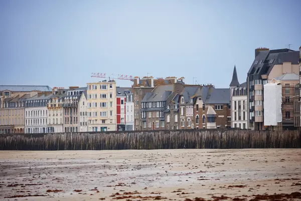Rıhtım boyunca uzanan tarihi binalar bulutlu gökyüzünün altında geniş bir sahile bakıyor Saint-Malo, Bretagne, Fransa