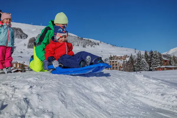 Genç kardeş, kardeşini dağdaki yamaçtan aşağıya itiyor. Kış oyunlarının tadını çıkarıyor.