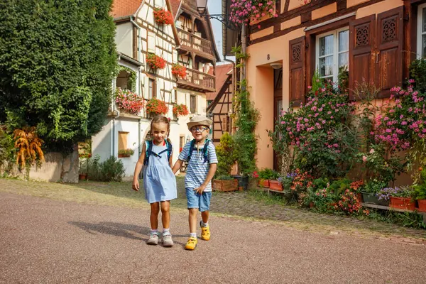 Sırt çantalı iki genç gezgin Avrupa, Alsace bölgesi, Fransa 'daki Eguisheim kasabasının kaldırım taşı sokaklarında maceralı bir yürüyüş yapıyorlar.