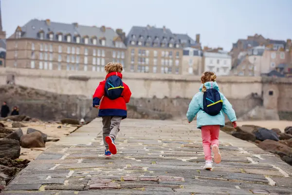 Bir çift çocuk sevinçle kaldırım boyunca koşuyor tarihi mimarisi ve arkadaki kayalık sahili ile Saint-Malo, Bretagne, Fransa