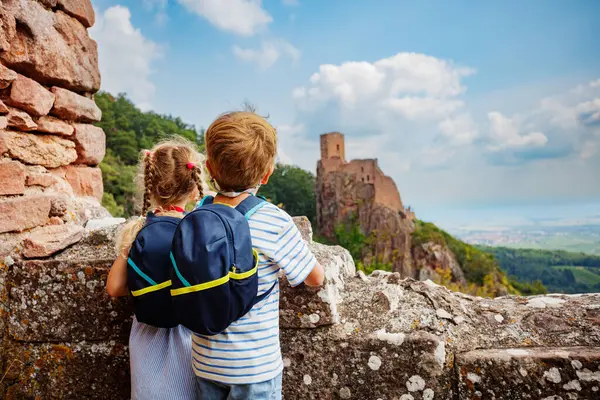 Bir oğlan ve kız sırt çantalarını takmış taş duvarda duruyorlar. Fransa 'nın uzak bir köşkündeki Girsberg Kalesi' nin kalıntılarına hayran bakıyorlar.