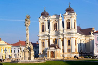 Romanya 'nın Timisoara kentindeki Aziz George Katolik Katedrali' nde, önplanda Kutsal Üçleme Anıtı, berrak mavi bir gökyüzünün altında güneş ışığıyla yıkandı..
