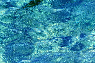 Kristal kadar berrak Adriyatik Denizi suyuna yakın çekim, soyut desenler ve güneş ışığı yansımaları, arka plan ve tasarım için mükemmel bir doğal doku yaratıyor..