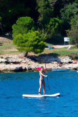 Bir kadın Adriyatik Denizi 'nde ayakta kürek çekme pratiği yapıyor. Spor tahtasında denge kuruyor, spordan zevk alıyor, eğlence ve dinamik düşüşlerle aksiyon ve mizah ekliyor..