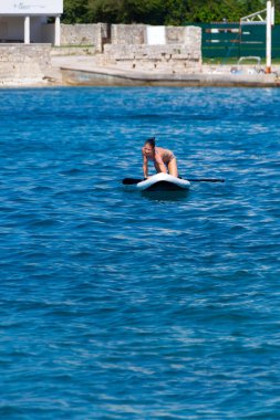 Bir kadın Adriyatik Denizi 'nde ayakta kürek çekme pratiği yapıyor. Spor tahtasında denge kuruyor, spordan zevk alıyor, eğlence ve dinamik düşüşlerle aksiyon ve mizah ekliyor..