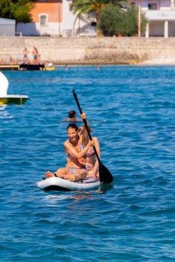 Anne ve kızı bir SUP tahtasına oturup Adriyatik Denizi 'nde kürek çekiyorlar. Eğlenceli aile bağları, yaz maceraları ve suda aktif bir yaşam tarzı..