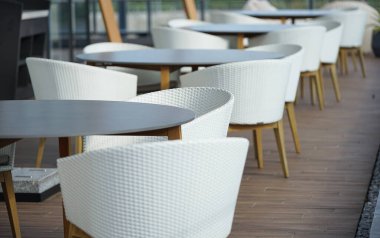 Kafede bir sürü masa ve beyaz sandalye var.                               