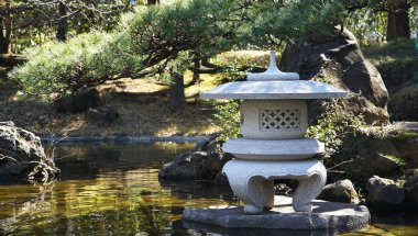 Japonya bahçesindeki gölette taş fenerlerin manzarası.                               