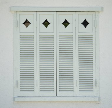 Evin dış tarafında beyaz pencere panjurları var.                               