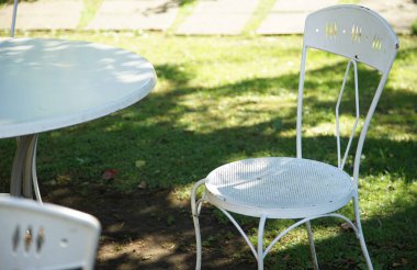 Güneşli bir günde çimenli bahçede beyaz masa ve sandalyeler.                               