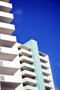 Miami Beach 'te daha eski bir apartman dairesi. Bir dizi balkonu var. Canlı, mavi bir gökyüzüne karşı. Mimari tasarım temiz çizgiler ve çarpıcı bir karşıtlık yaratan açık mavi renkler içerir.,