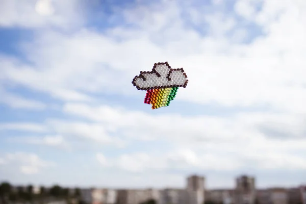 A cloud and a rainbow made of pearls on the background of the sky and houses. Abstract background