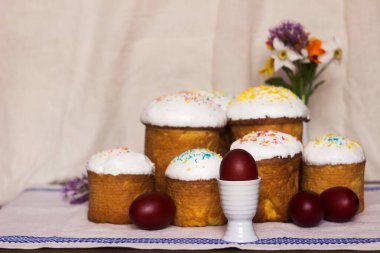 Paskalya ekmekleri, üzerinde krema ve renkli serpiştirilmiş Paskalya yumurtaları ve bahar çiçekleri olan bir masa. Metin için yer