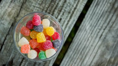 Dışarıdaki ahşap masada, camların içinde renkli şekerler.