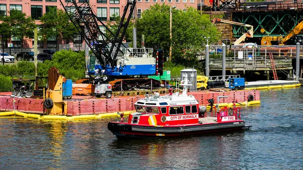 stock image NORWALK, CT, USA - JUNE 15, 2024:  A red fireboat with the words City of Norwalk  next to a construction site with a large crane and other equipment