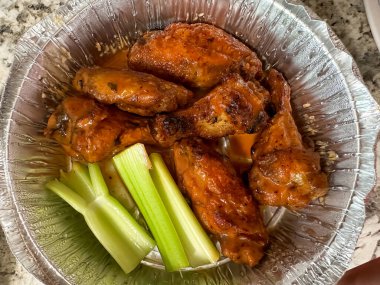 Baharatlı tavuk kanatlarının lezzetli bir porsiyonu parlak bir folyo kabında sunulan taze kereviz çubuklarıyla eşleştirilir. Kanatlar mükemmel pişmiş, aromalarını ön plana çıkaran zengin turuncu bir jöle sergiliyorlar..