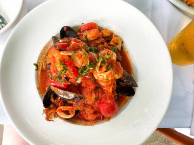 Taze karides, midye ve domatesli canlı bir deniz ürünleri makarnası zarif bir şekilde beyaz bir kasede sunuluyor..