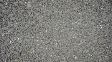 Yüzeyde, renk ve dokudaki doğal değişimleri yansıtan küçük, yuvarlak taşlar ve çakıllar sergileniyor.