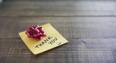 Minnettarlığımızı ifade eden el yazısıyla yazılmış bir not küçük kırmızı bir fiyonk eşliğinde ahşap bir masaya konur.