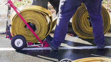 NORWALK, CT, USA - NOVEMBER 1, 2024: A firefighter stands on pavement, rolling up a hose on a cart. clipart