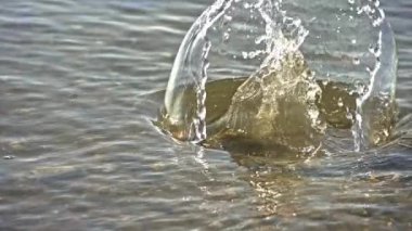 Bacakları ağır çekimde sığ sularda yüzen bir adam. Su dalgalanıyor ve güneş ışığını yansıtıyor.