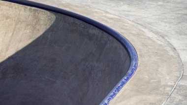 Kıvrımlı bir kaykay kasesi, gün ışığında bir şehir kaykay parkında yer alan pürüzsüz bir yüzeye ve gölgeli kenarlara sahiptir..