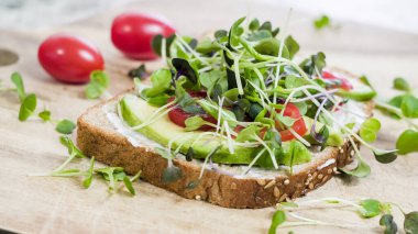 Mayonez, avokado, domates ve çeşitli mikro yeşilliklerle kaplı bir dilim tam buğday ekmeği.