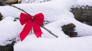 A vibrant red ribbon is tied to a bare branch, resting on fresh, untouched snow in a tranquil winter setting. clipart