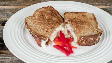 Lezzetli bir ızgara peynirli sandviç, erimiş peynirle birlikte mükemmel bir yemek için dilimlenmiş taze kırmızı biberle bir tabakta oturur..