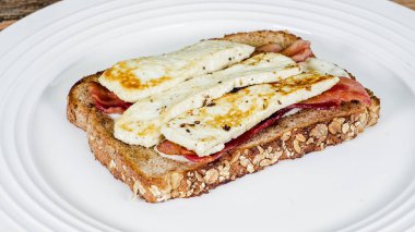 Açık yüzlü bir sandviçin içinde domuz pastırması ve kızarmış peynir ve sağlıklı yulaf ekmeği bulunur. Öğle yemeği ya da hafif bir yemek için mükemmeldir..