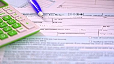 Bireyler, 2024 dosya sezonuna hazırlanmak için vergi formlarının karmaşıklığında geziniyorlar. Bir hesap makinesi ve kalem doğruluk ve detayların önemini vurgular.
