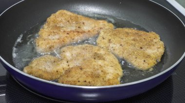 Üç parça tavuk tavada kızarıyor ve altın-kahverengi bir kabuk oluşturuyor. Tavuğun etrafında sıcak yağ kabarcıkları oluşmakta olan lezzetli bir yemeği gösteriyor..