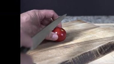 Yetenekli bir insan, tahta kesme tahtasında keskin bir bıçakla taze domates kesme sanatını sergiliyor. Odaklanma tekniği ve canlı renkler üzerine.