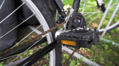 Bir bisiklet pedalı belirgin bir şekilde zincir ve çevreleyen yeşillik üzerine odaklanarak sergilenir.