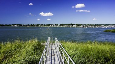 NORWALK, CT, ABD 27 AĞUSTOS 2025 Sakin sulara açılan uzun bir rıhtım manzarası. Bereketli yeşil çimenler, açık mavi gökyüzünün altında körfez boyunca görülebilen pitoresk evler ile bölgeyi çevrelemektedir.