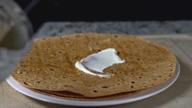 Flatbread is prepared with care on a wooden surface, showcasing its thin texture. A generous layer of fresh mayonnaise is spread across, enhancing the flavor.