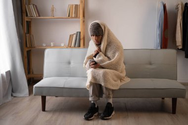 Battaniyeli sağlıksız bir adam soğuk oturma odasında oturur cep telefonu kullanır. Isı ve güç eksikliğinden muzdariptir. Sağlıksız genç adam evdeki dondurucu soğuktan mücadele ediyor. Isıtma kavramı yok.