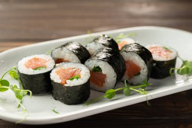 Masaki beyaz tabakta somon balığı ile sıraya dizildi. Pirinç ve nori ile taze hosomaki parçaları. Nefis Japon yemeklerini suşili dürüm ile kapatın..