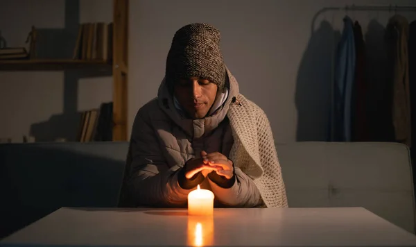 Young man without electricity at home with candle. Shutdown of heating and electricity, power outage, blackout, load shedding or energy crisis. copy space.