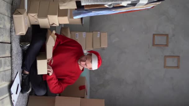 サンタクロースの帽子をかぶった髭の男はクリスマスのためのオンラインストアからの贈り物や注文と箱の家で動作します 小規模事業主は幸せな新年を販売しています 配達の休日だ 垂直ビデオ — ストック動画
