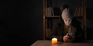 Avrupa 'da yaşanan bir enerji krizi sırasında ısıtma ve elektrik kesintisine uğrayan genç bir kadın görülüyor. Haberleri okumak için akıllı telefonu kullanmak. Kışın evde ısıtma yok. Pankart