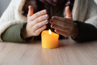 Sıcak giysiler içinde yanan mumdan ısınan kadınların ellerini yakın. Oturma odasında. Kış, ısınma mevsimi, sıcaklık kavramı yok