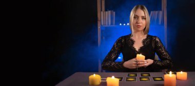 Tarot kartları okuyan bir falcı elinde mumla oturur, bir kadın kahin ise karanlık bir odada. Ayin mumlarının yanması, ruh çağırma, duman. Pankart