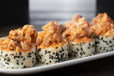 Japon suşi volkanı yılan balığıyla yuvarlanıyor, üstünde uçan balıklar ve içinde susam, yan görüş. Beyaz tabakta servis edilmiş. Koyu arkaplan