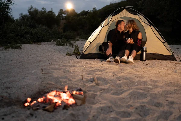 romantic couple on camping on sea shore of evening starry sky. Tourist couple, man and woman hikers sitting at bonfire. Copy space