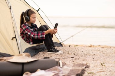 Deniz kıyısında tatil yapan genç bir turist. Mutlu genç kız kamp çadırında dinleniyor. Yürüyüş çocuğu telefondan müzik dinle. Sağlıklı, aktif yaşam tarzı olan insanlar. Boşluğu kopyala