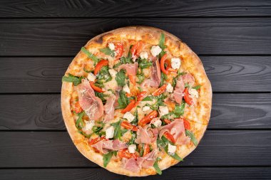 Parma jambonlu pizza, mozzarella peyniri roka, koyu arkaplanda vişneli domates. Ahşap manzaralı geleneksel İtalyan pizzası. Boşluğu kopyala