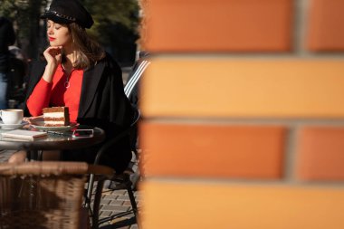 Şık siyah şapkalı genç turist kadın ve sonbahar parlak kırmızı kazağı caddedeki kafede oturuyor ve gün ışığında harika bir tatil yapıyor. Metin için boşluk