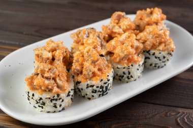 Japon suşi volkanı, üstünde yılan balığı ve içinde susam var. Beyaz tabakta servis edilmiş. Koyu ahşap arka plan. Suşi menüsü